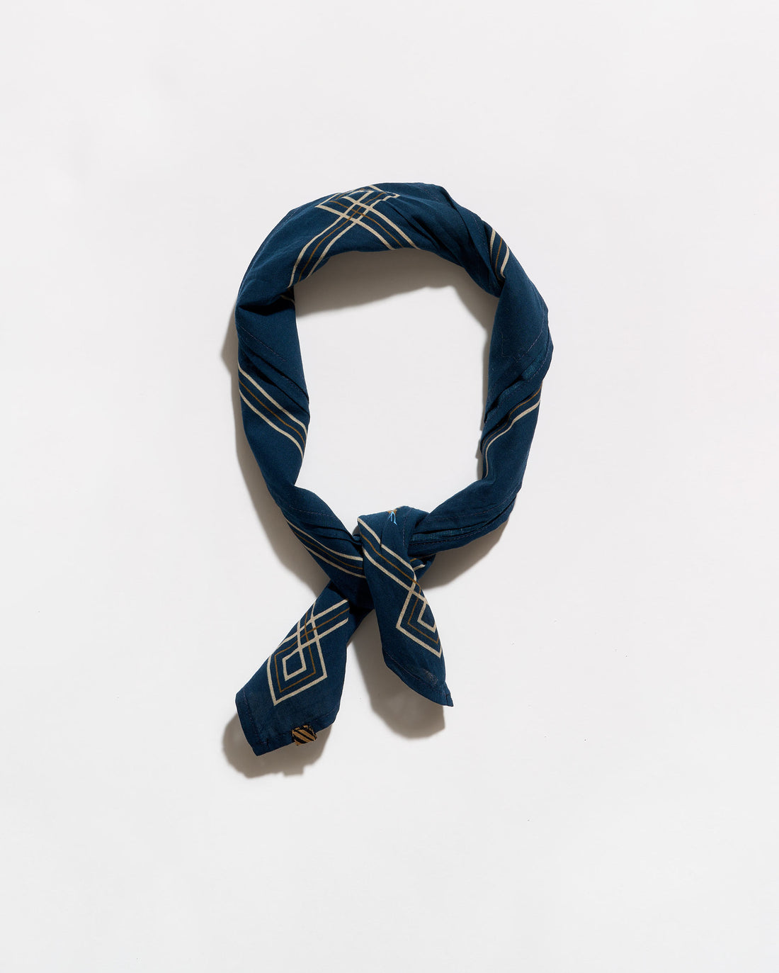 A navy blue silk scarf with a white geometric pattern, tied in a loop and knot, displayed on a clean white background.