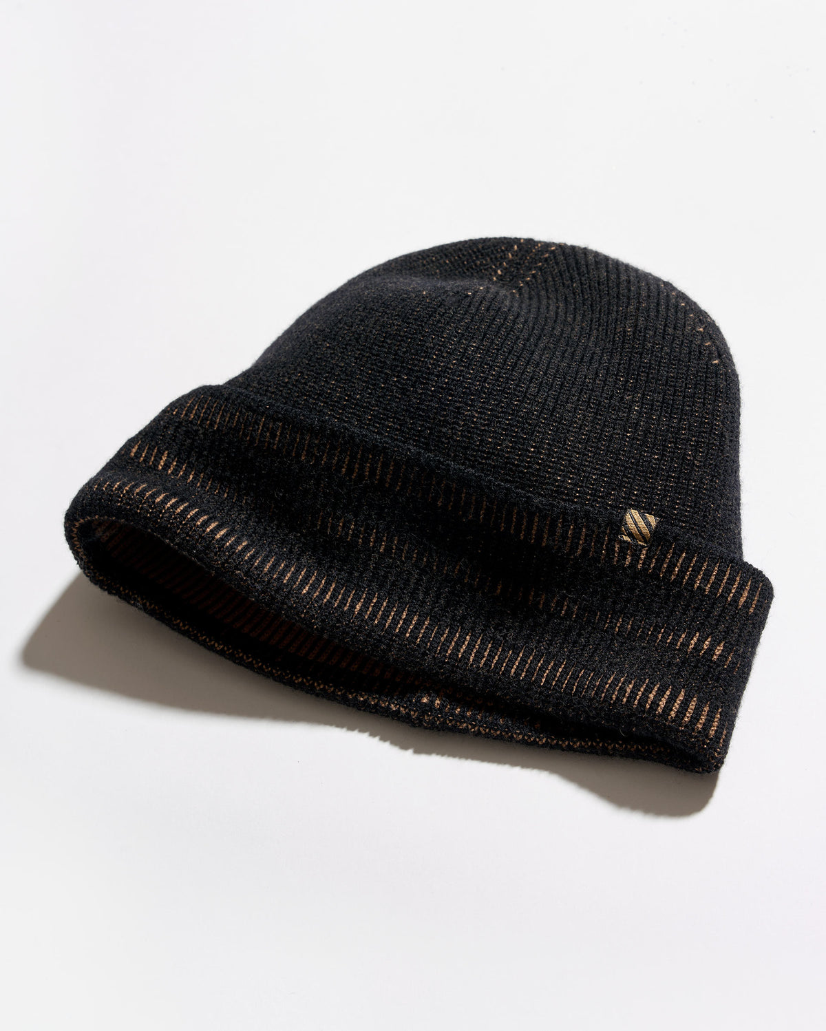 A black knit beanie hat with a folded cuff, featuring a small gold embroidered logo on the side, photographed on a clean white background with a soft shadow.