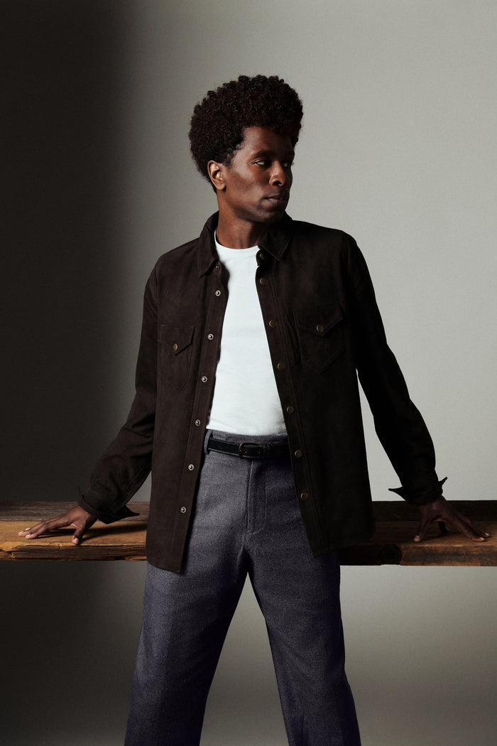 Man wearing a dark jacket and white shirt against a neutral background