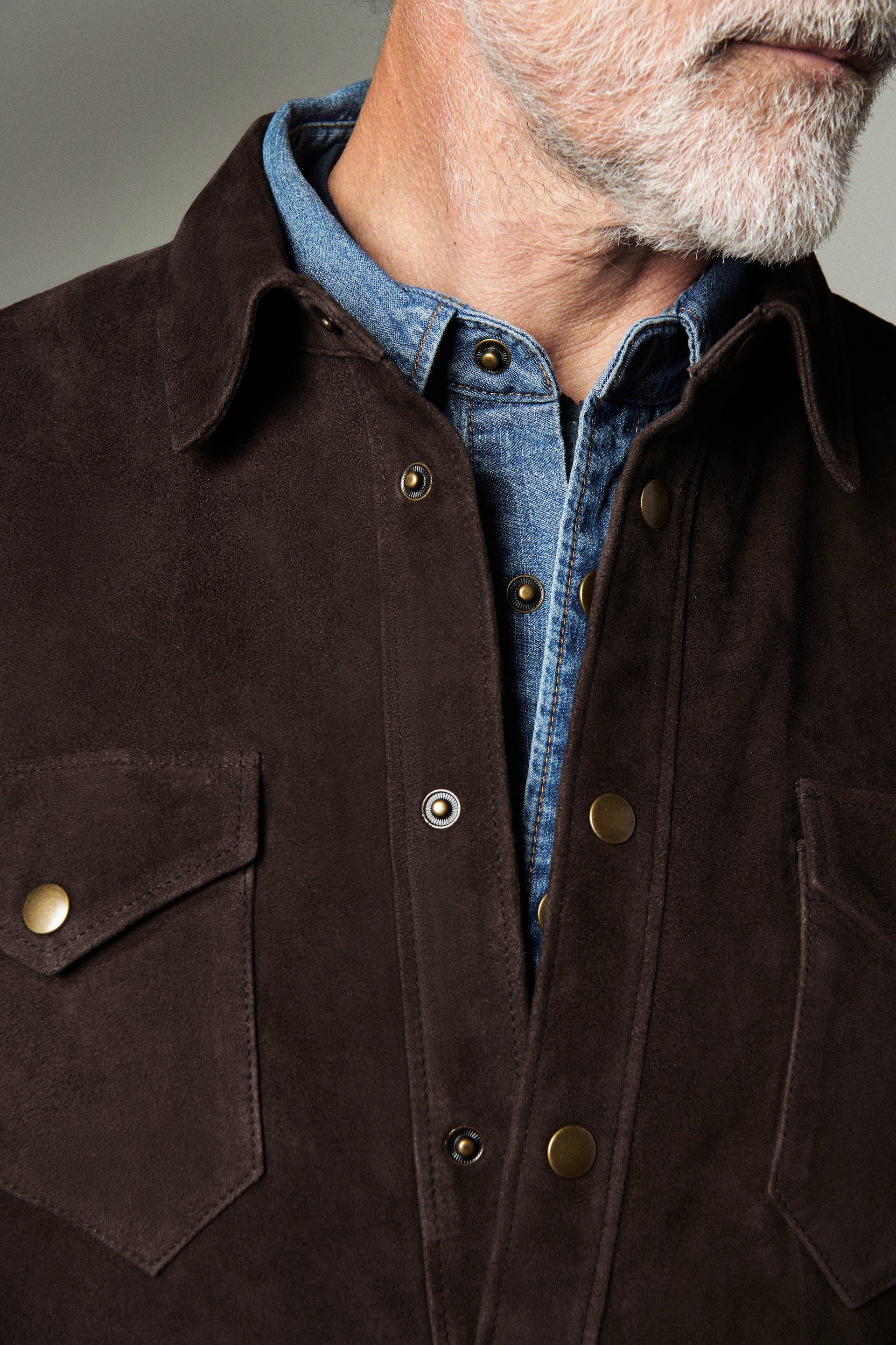 Close-up of a person wearing a dark brown jacket with a blue shirt underneath.