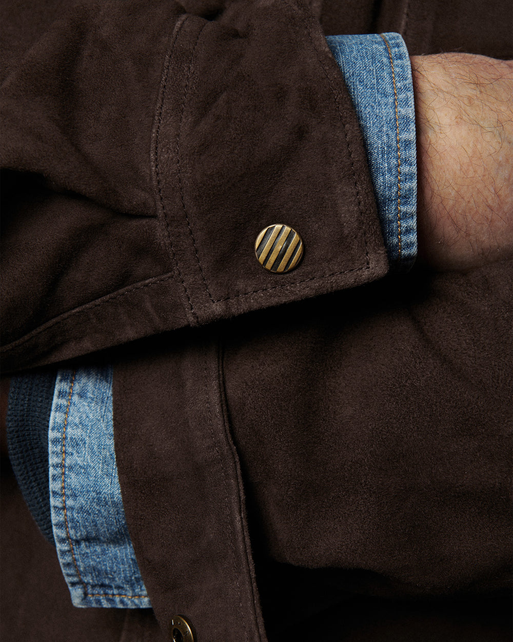 Close-up of a brown jacket with blue denim trim and gold button.