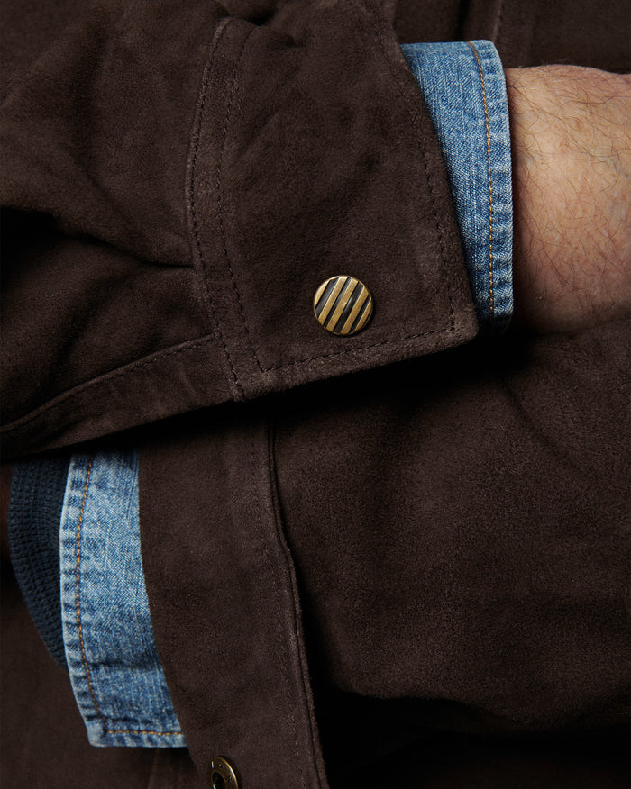 Close-up of a brown jacket with blue denim trim and gold button.