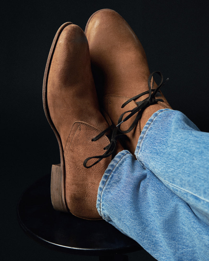 Brown leather shoes with black laces worn with blue jeans on a black background Alternate