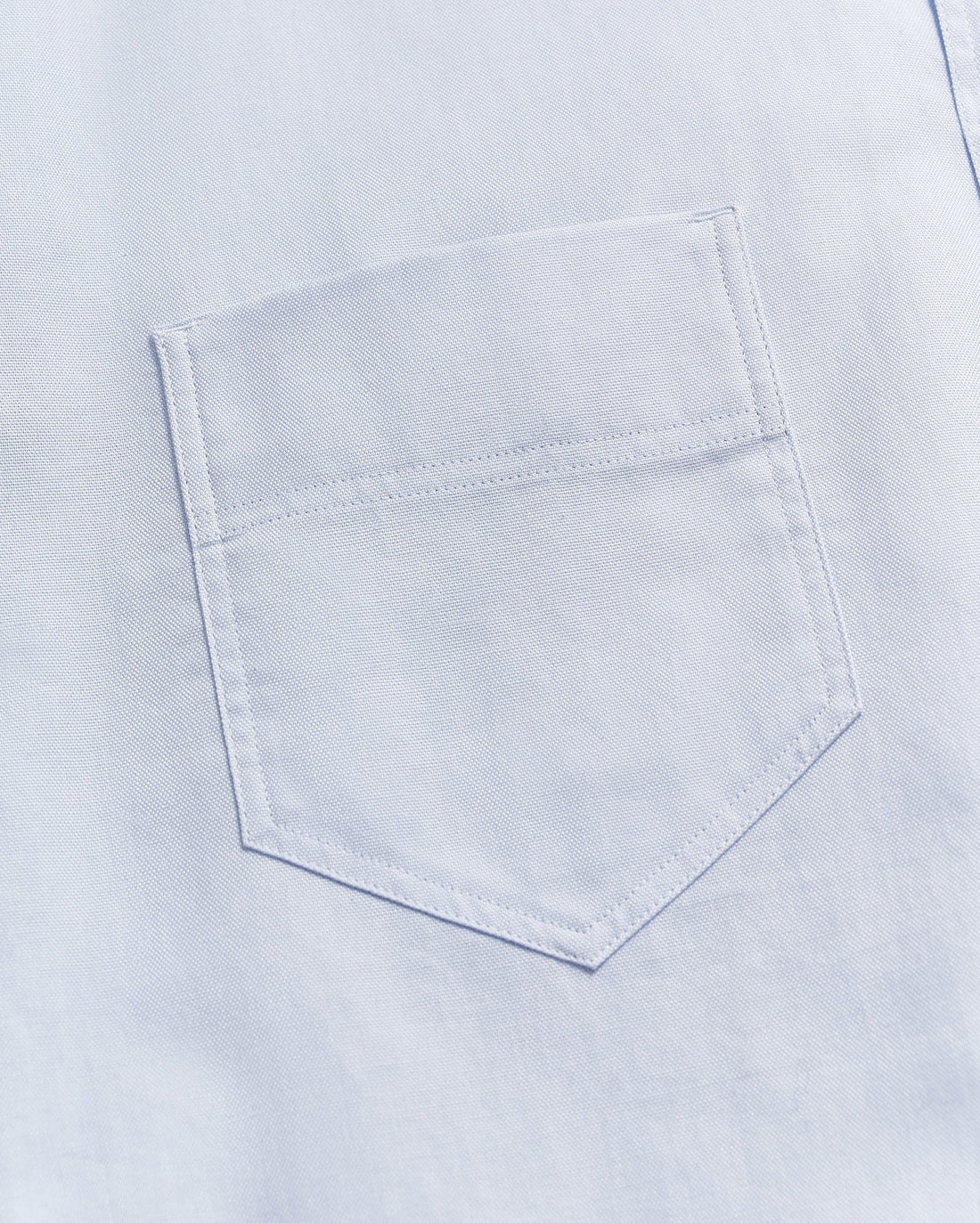 Close-up of a light blue fabric with a single, neatly stitched chest pocket visible in the center of the image.