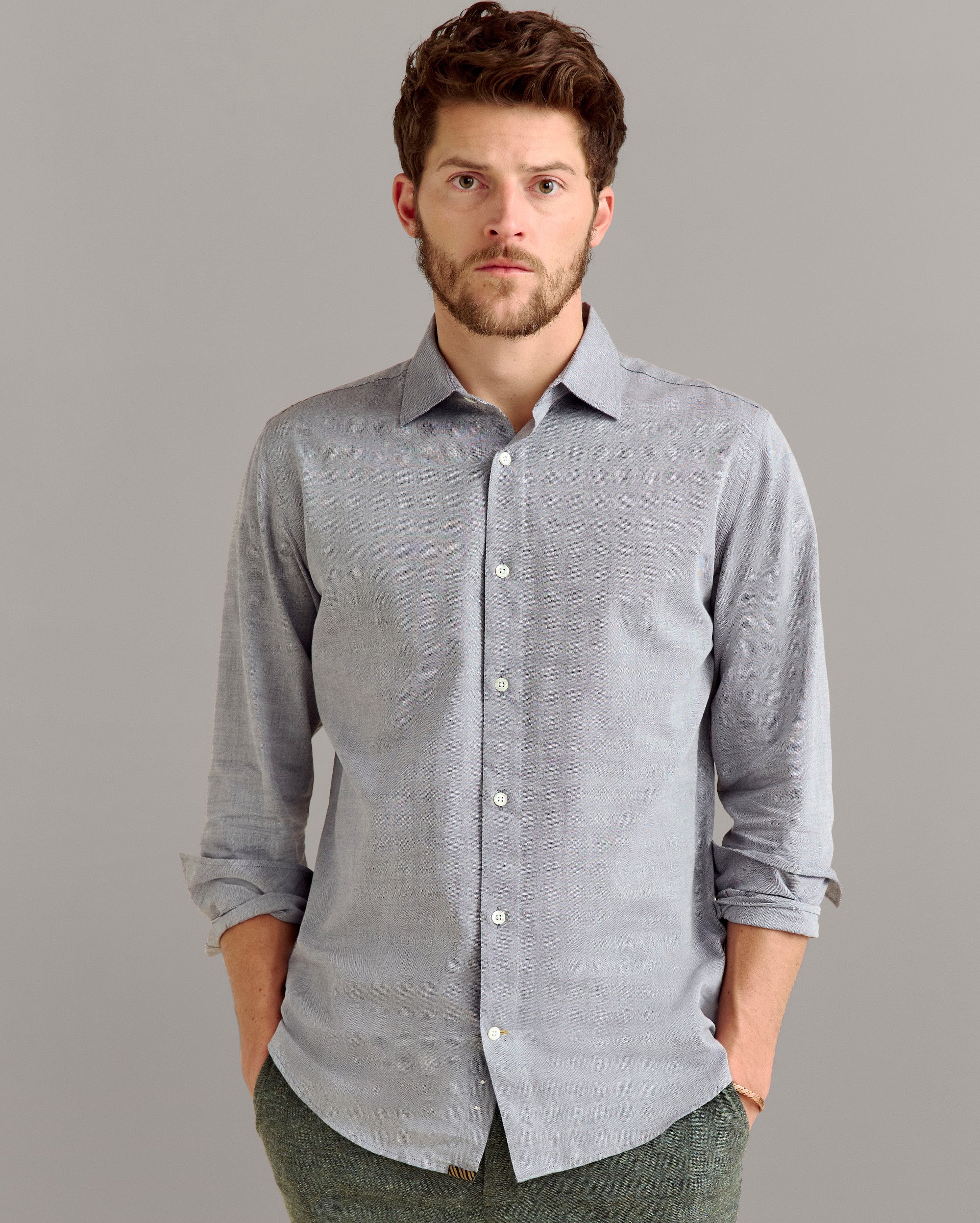 Man wearing a light gray button-up shirt against a gray background
