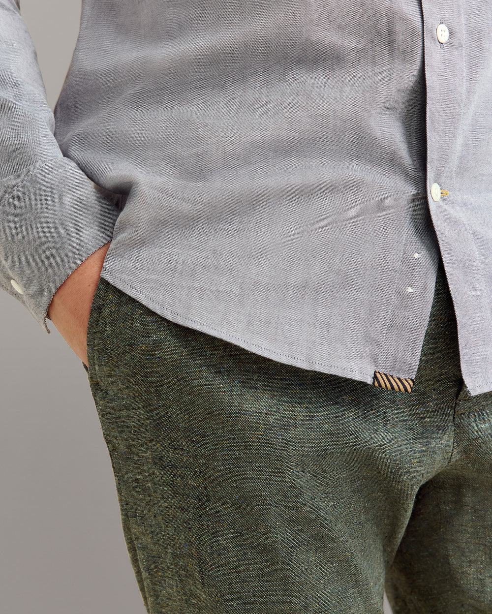 Person wearing a gray shirt and green pants against a plain background