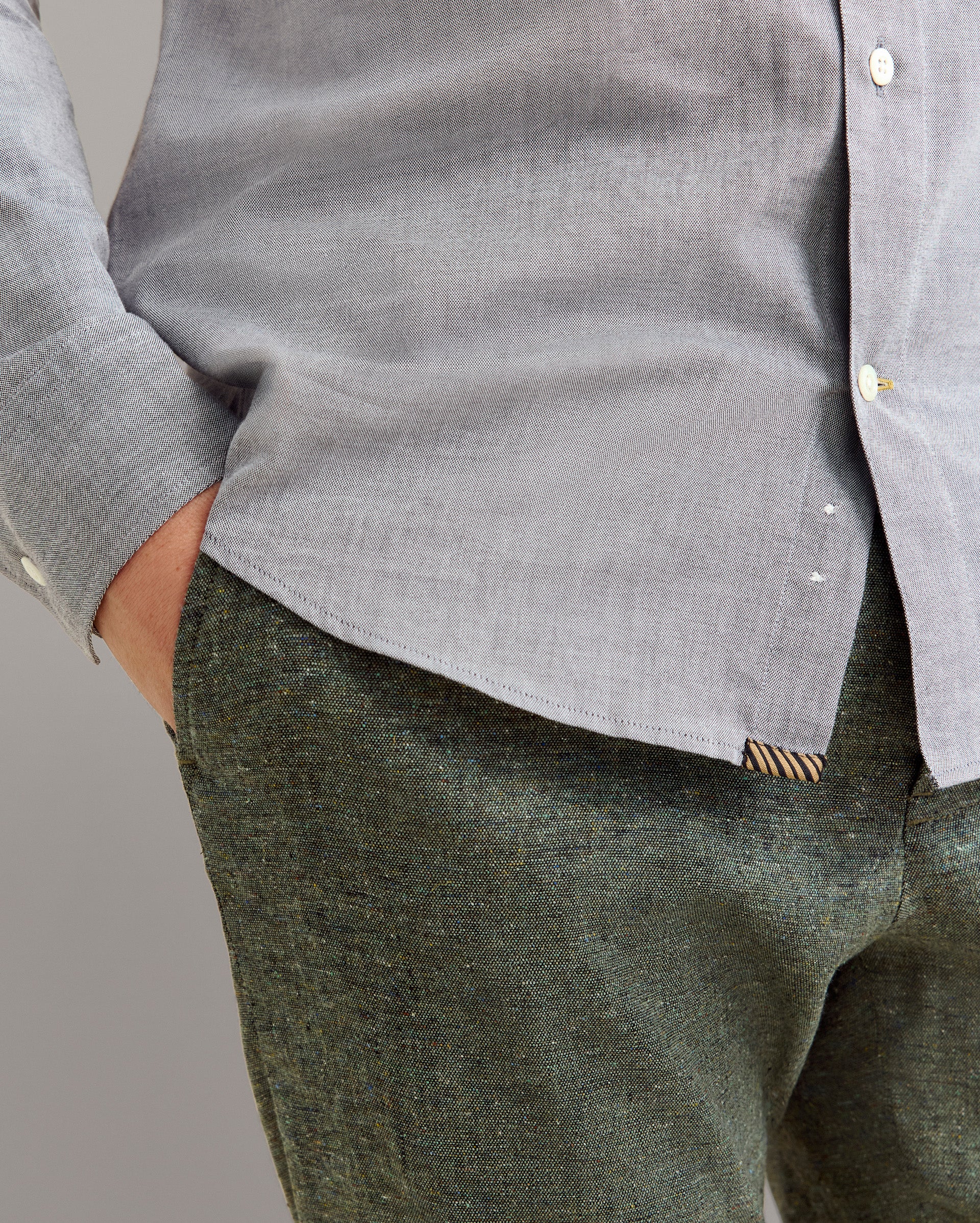 Person wearing a gray shirt and green pants against a plain background