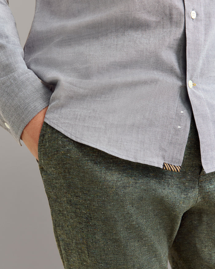 Person wearing a gray shirt and green pants against a plain background