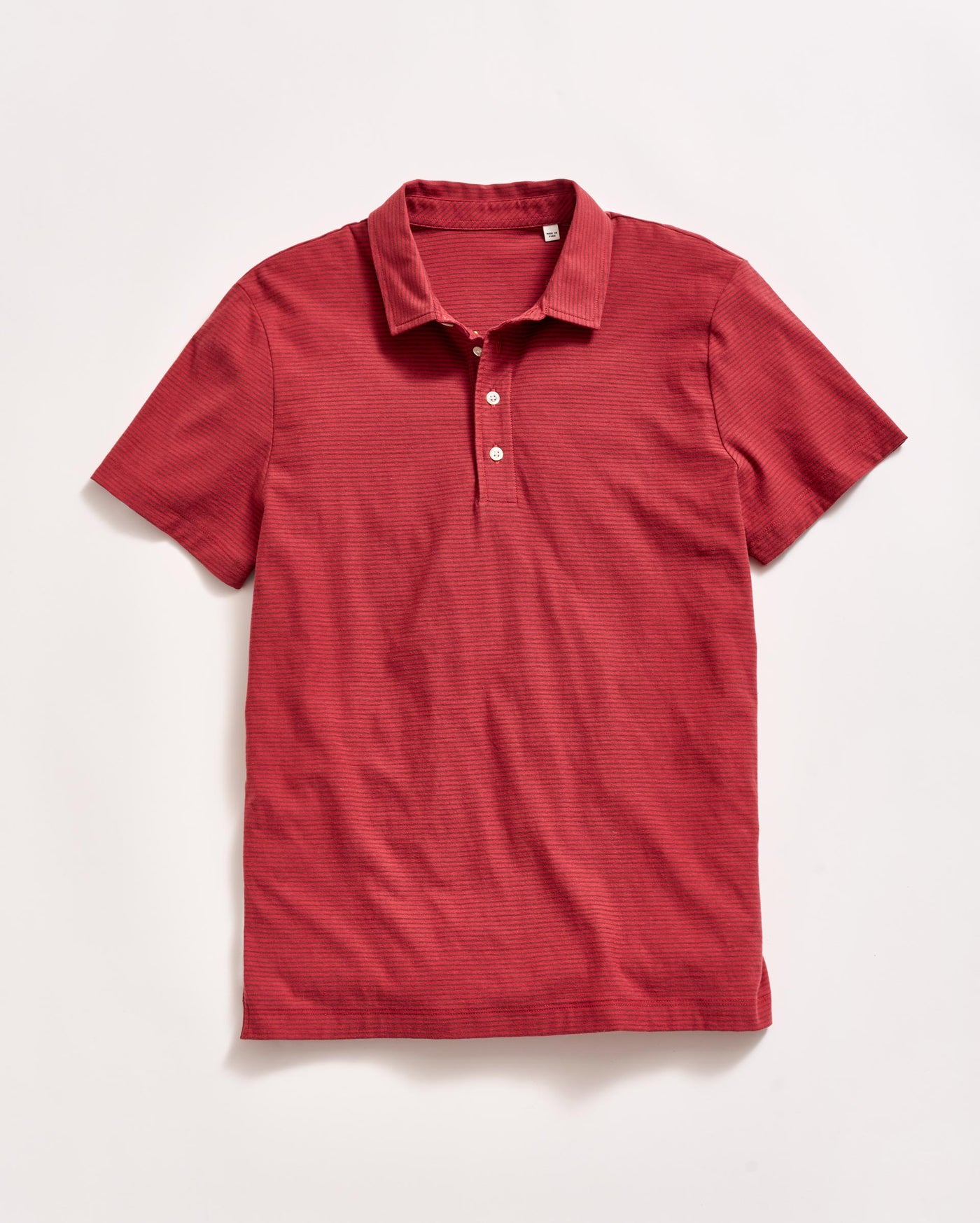 A short-sleeve, red polo shirt with a collar and three white buttons, laid flat on a white background.