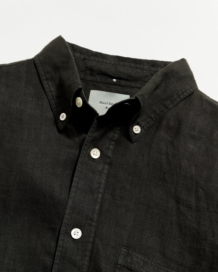Close-up of a black button-up shirt with a visible brand label on a light gray background