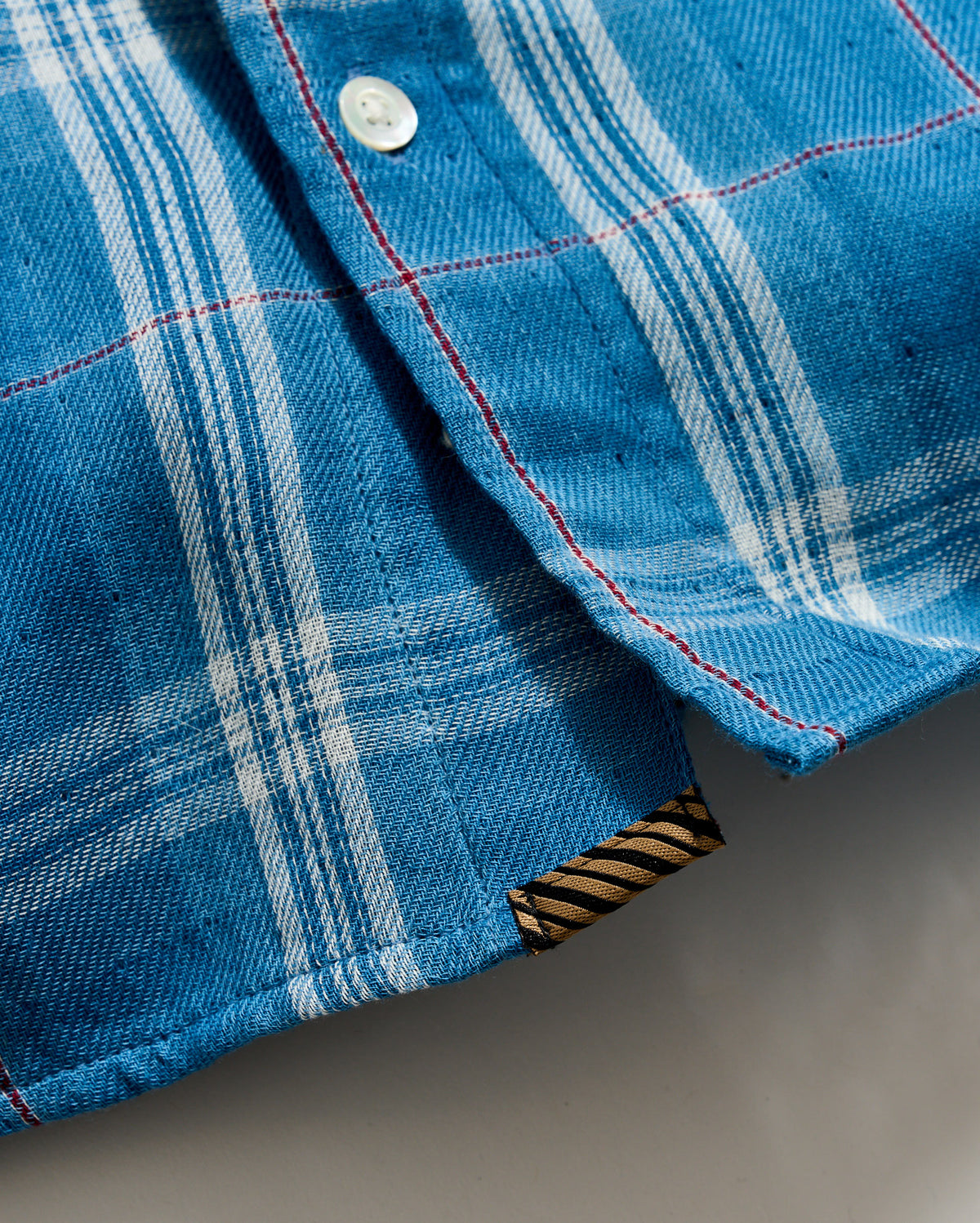 Close-up of a blue plaid fabric with a button and striped trim.