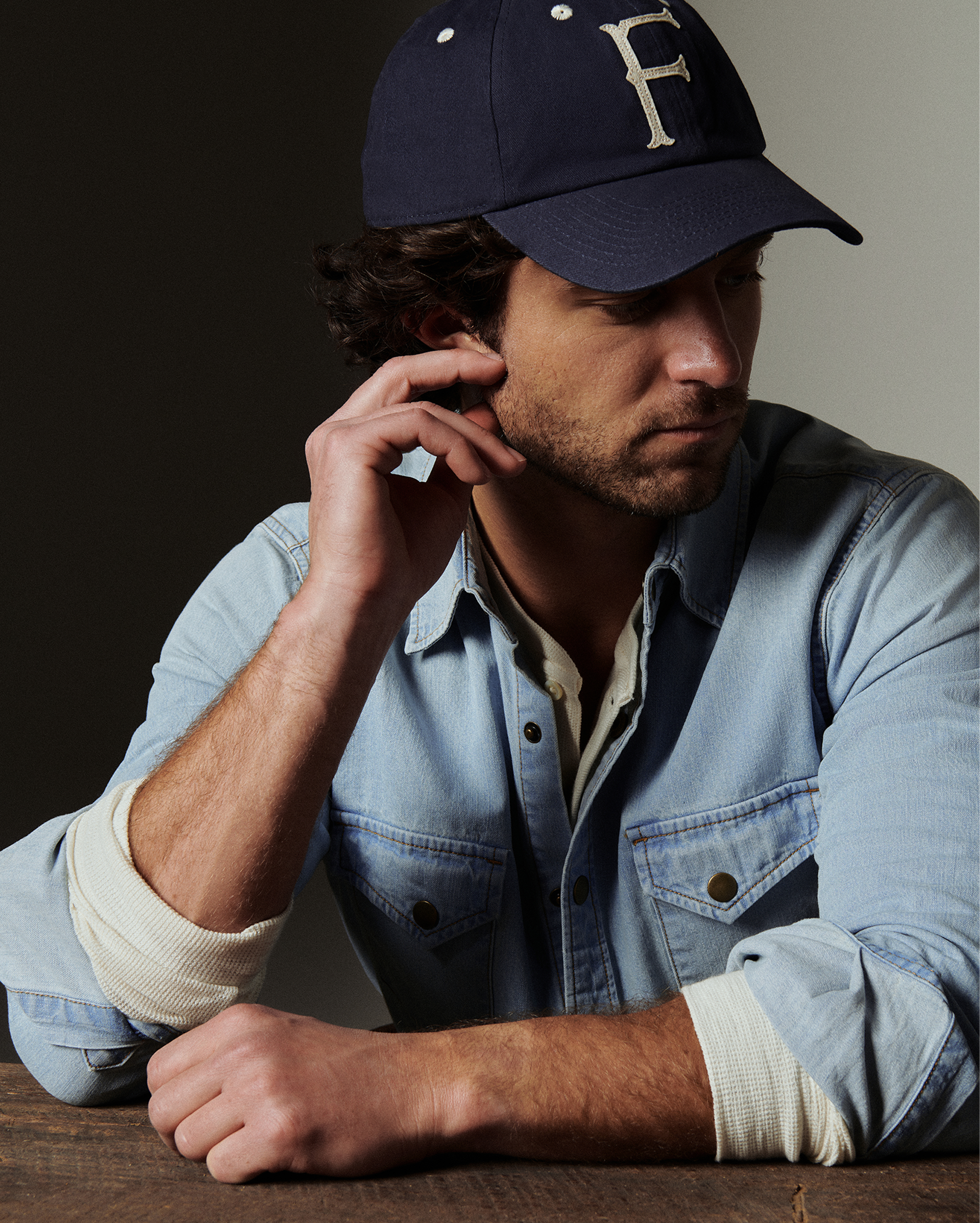 Man wearing a navy cap with a letter 'F' and a denim jacket, sitting at a table.