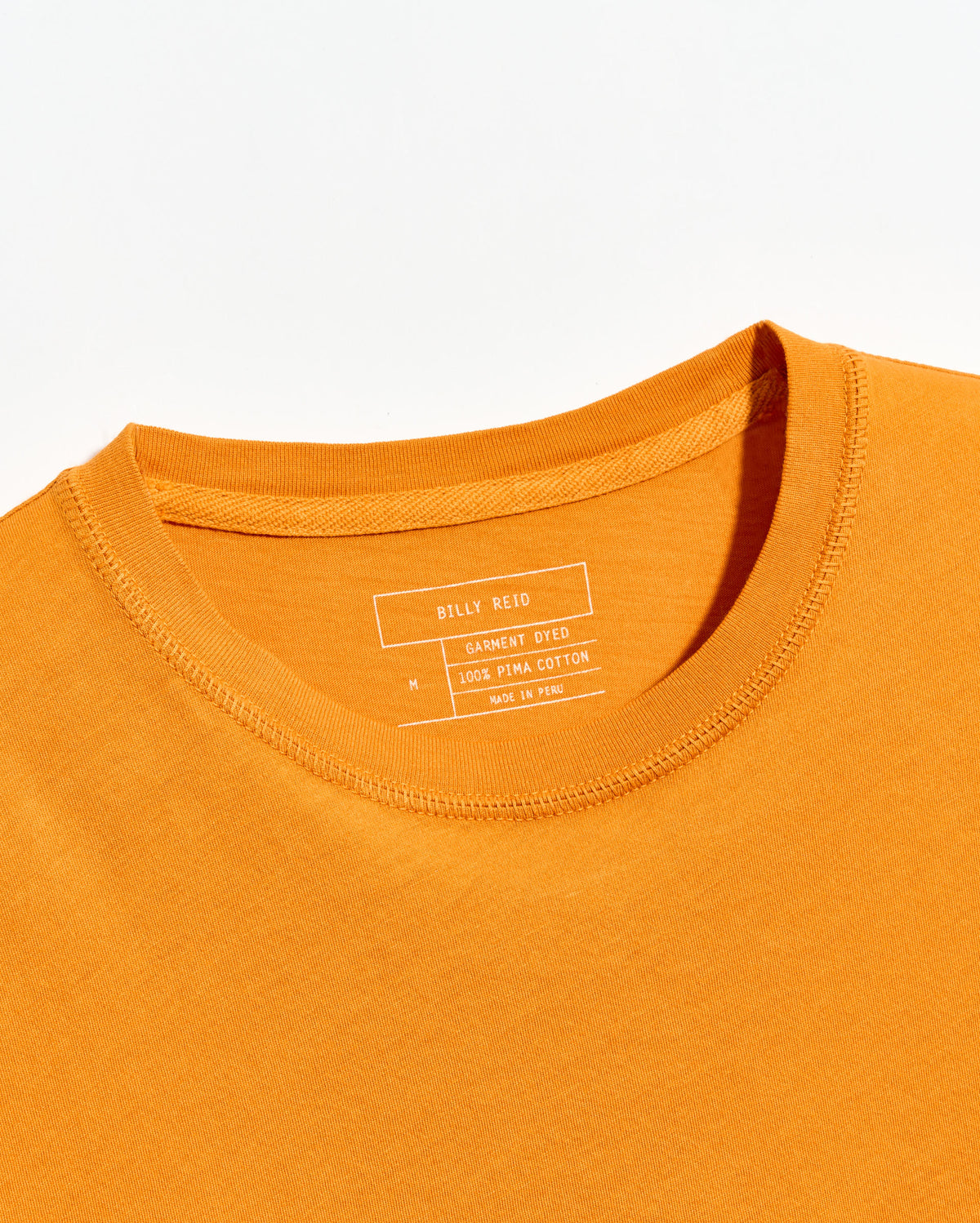 Close-up of an orange t-shirt with a brand label on a white background