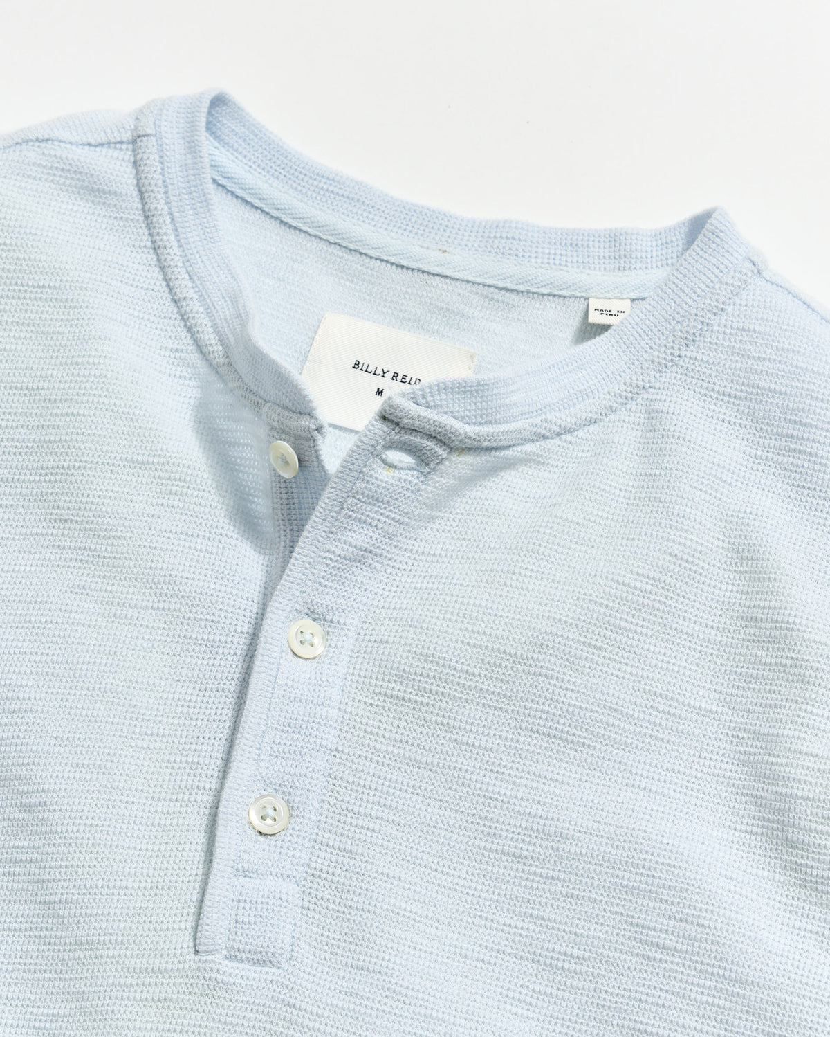 Light blue textured shirt with buttons and a visible brand tag on a light gray background