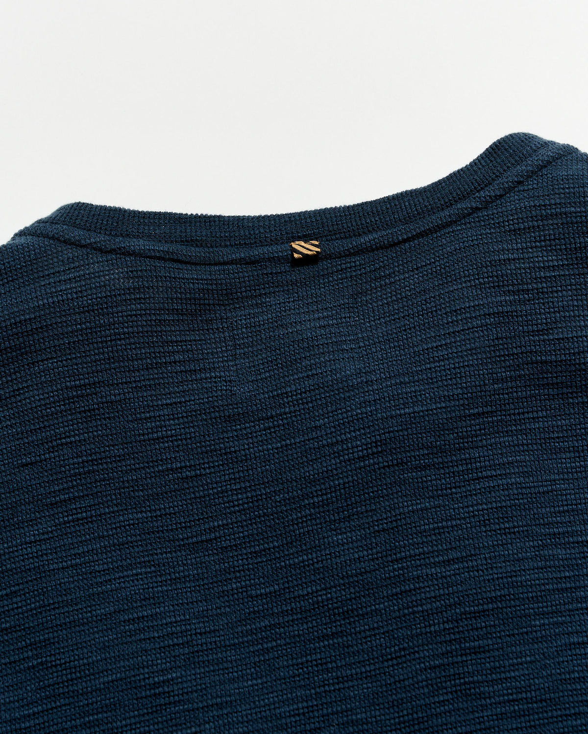Close-up of a dark blue garment with a brand logo on a light gray background