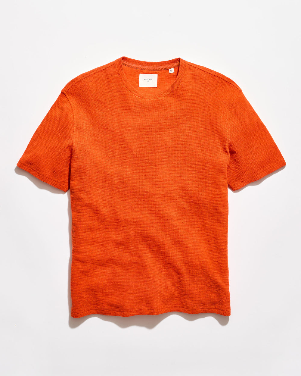 Orange crew neck shirt on a grey background.