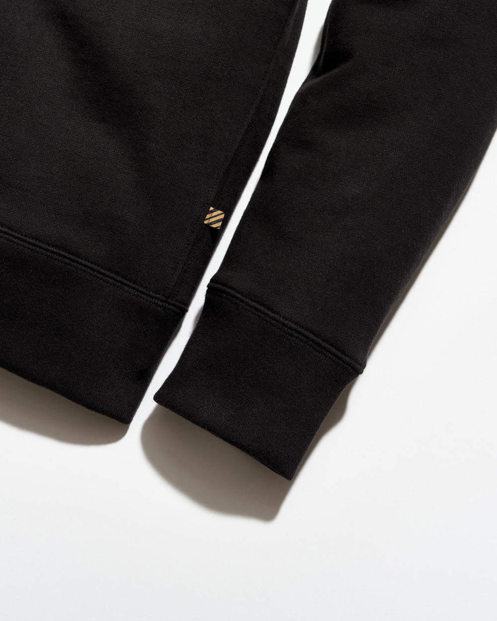 Close-up of a black sweatshirt with a brand logo on the sleeve against a white background