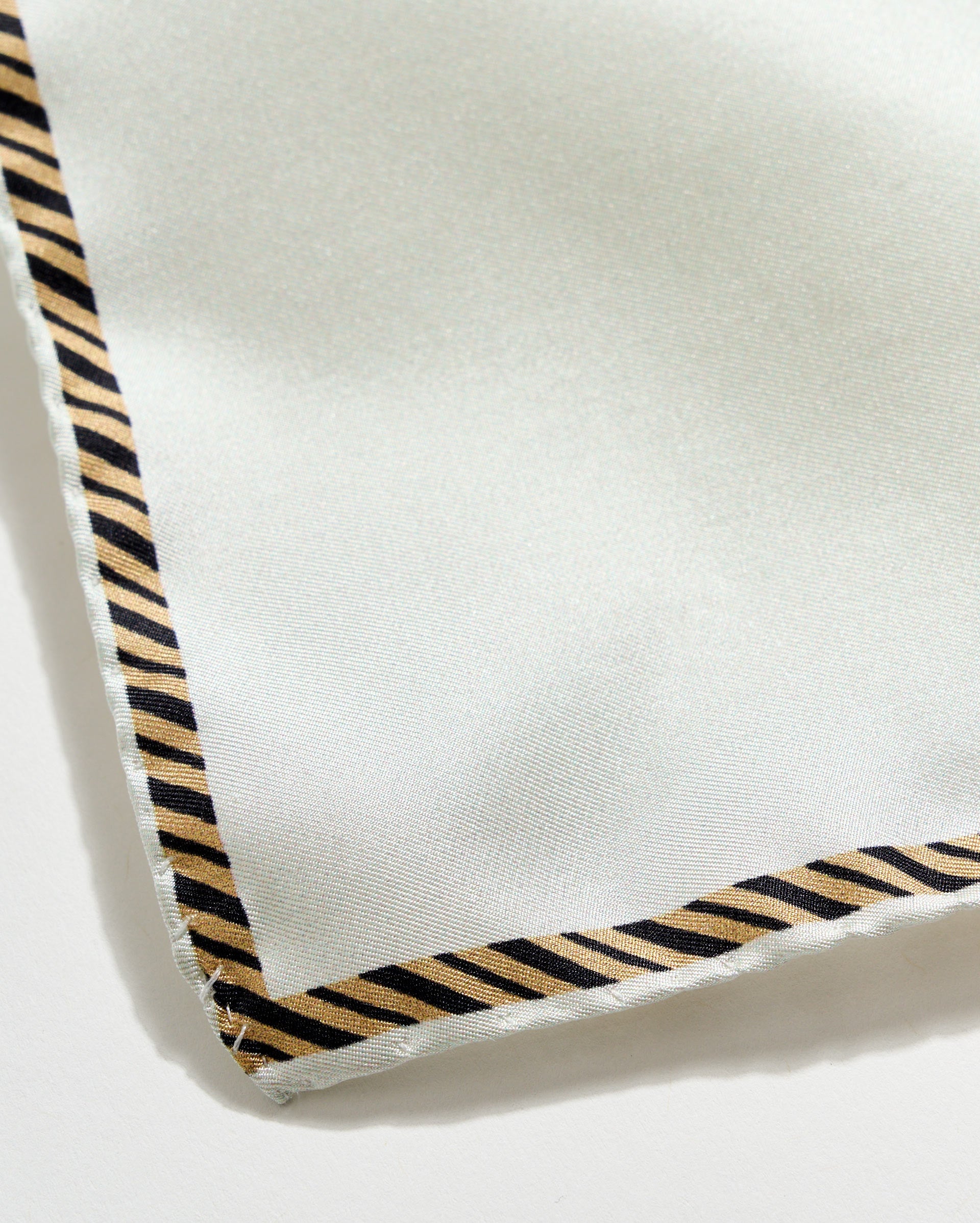 Close-up of a white fabric with black and beige striped border on a light gray background