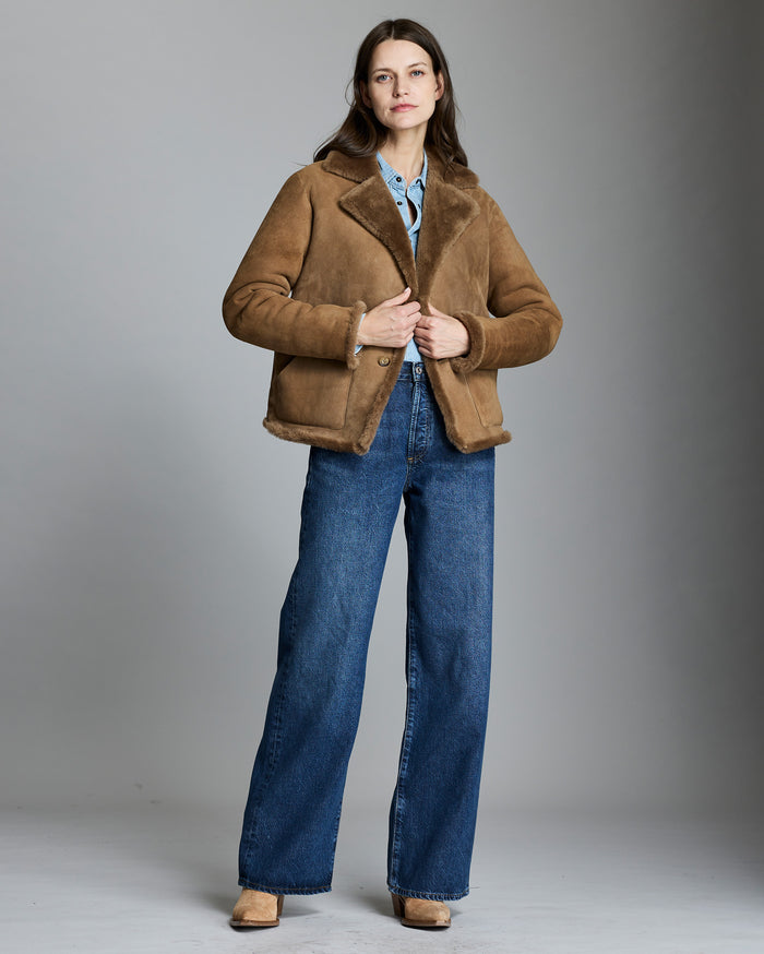Woman wearing a brown shearling jacket and blue jeans on a gray background
