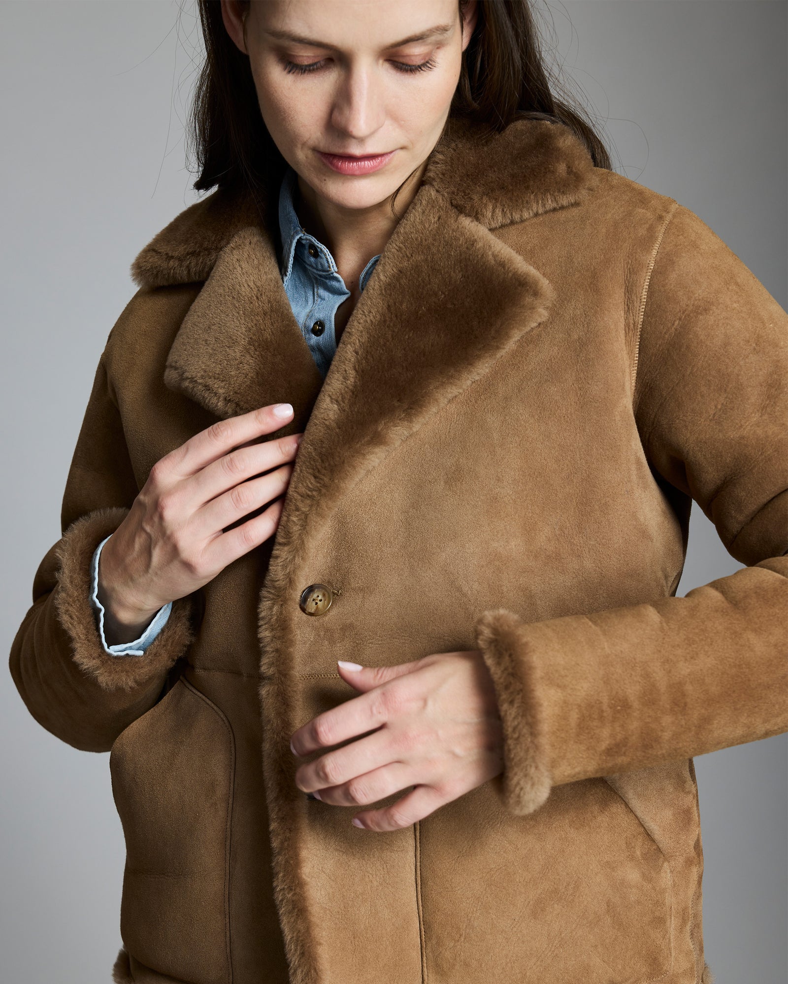 Woman wearing a brown shearling coat against a gray background