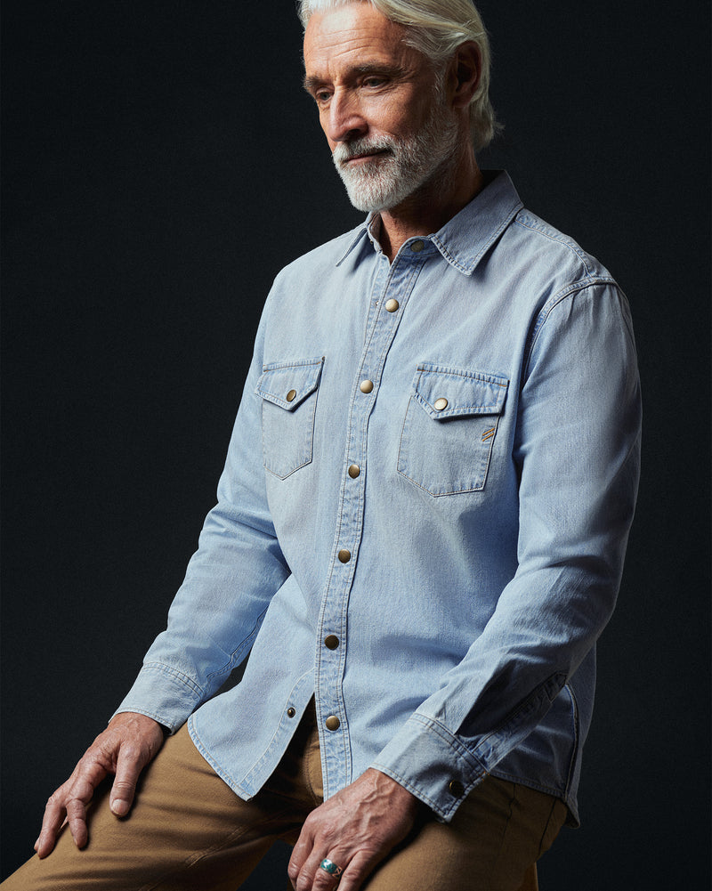 Man wearing a light blue denim shirt against a black background Alternate
