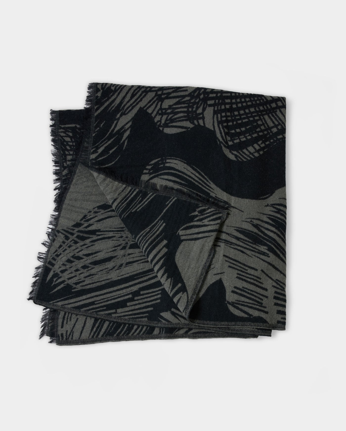 A folded black and gray scarf with an abstract, textured pattern and fringed edges, displayed on a plain white background.