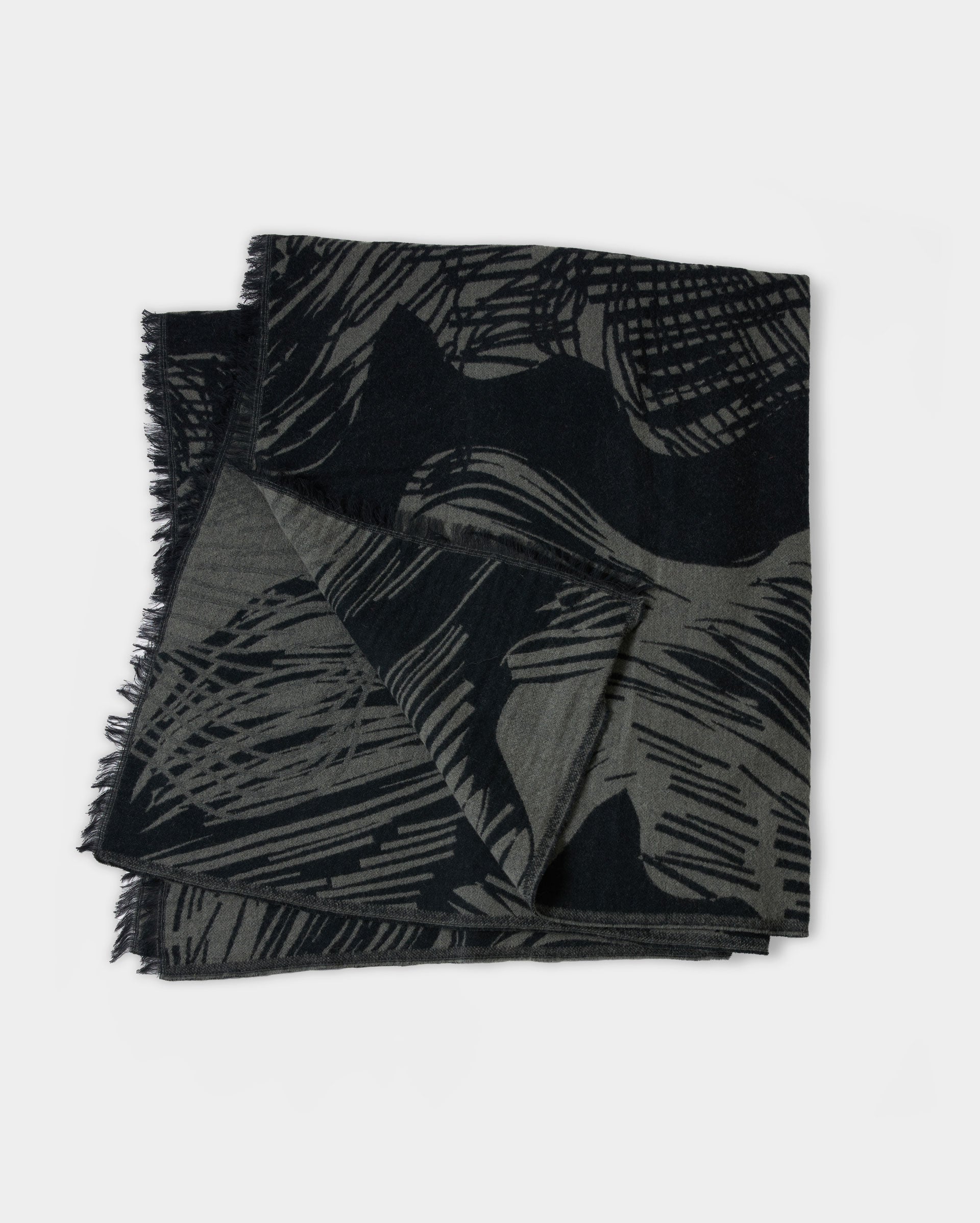 A folded black and gray scarf with an abstract, textured pattern and fringed edges, displayed on a plain white background.