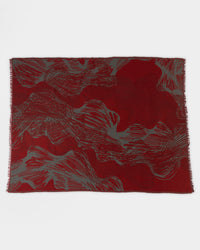 A rectangular textile with an abstract pattern in deep red and gray tones, featuring wavy, swirling lines across the surface and lightly fringed edges.