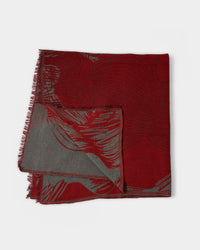 A folded, rectangular scarf with fringed edges. The scarf features a red and gray abstract pattern, with the red side more prominent on top and the gray side partly visible underneath.