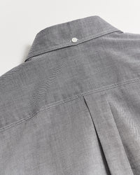 Close-up of the back of a gray button-up shirt featuring a box pleat and a small white button at the top near the collar, showcasing the shirts stitching and fabric texture.