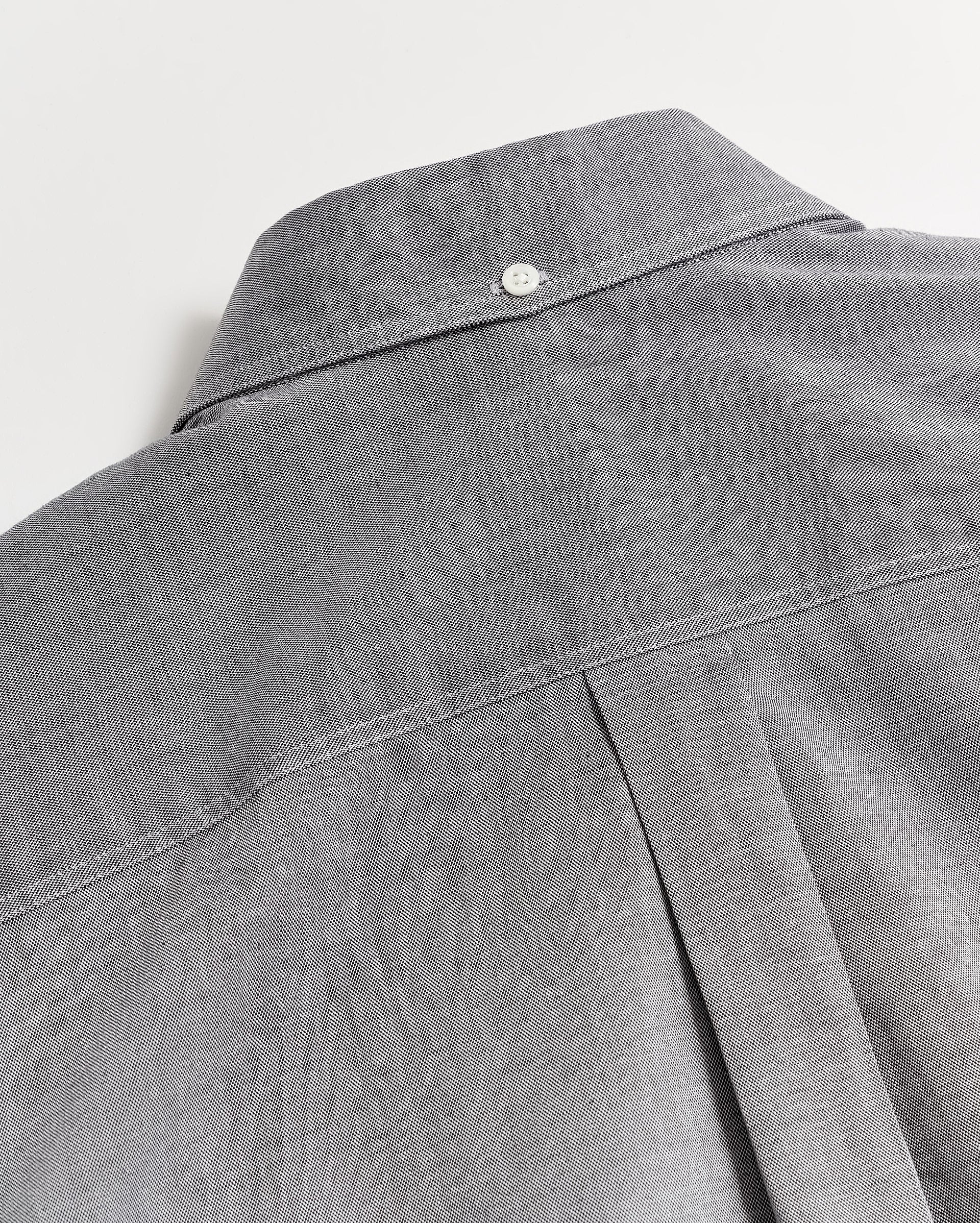 Close-up of the back of a gray button-up shirt featuring a box pleat and a small white button at the top near the collar, showcasing the shirts stitching and fabric texture.