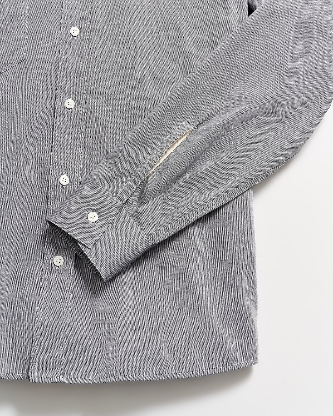 A close-up of a light gray button-up shirt with white buttons, showing the sleeve and part of the shirts front laid flat on a white surface.