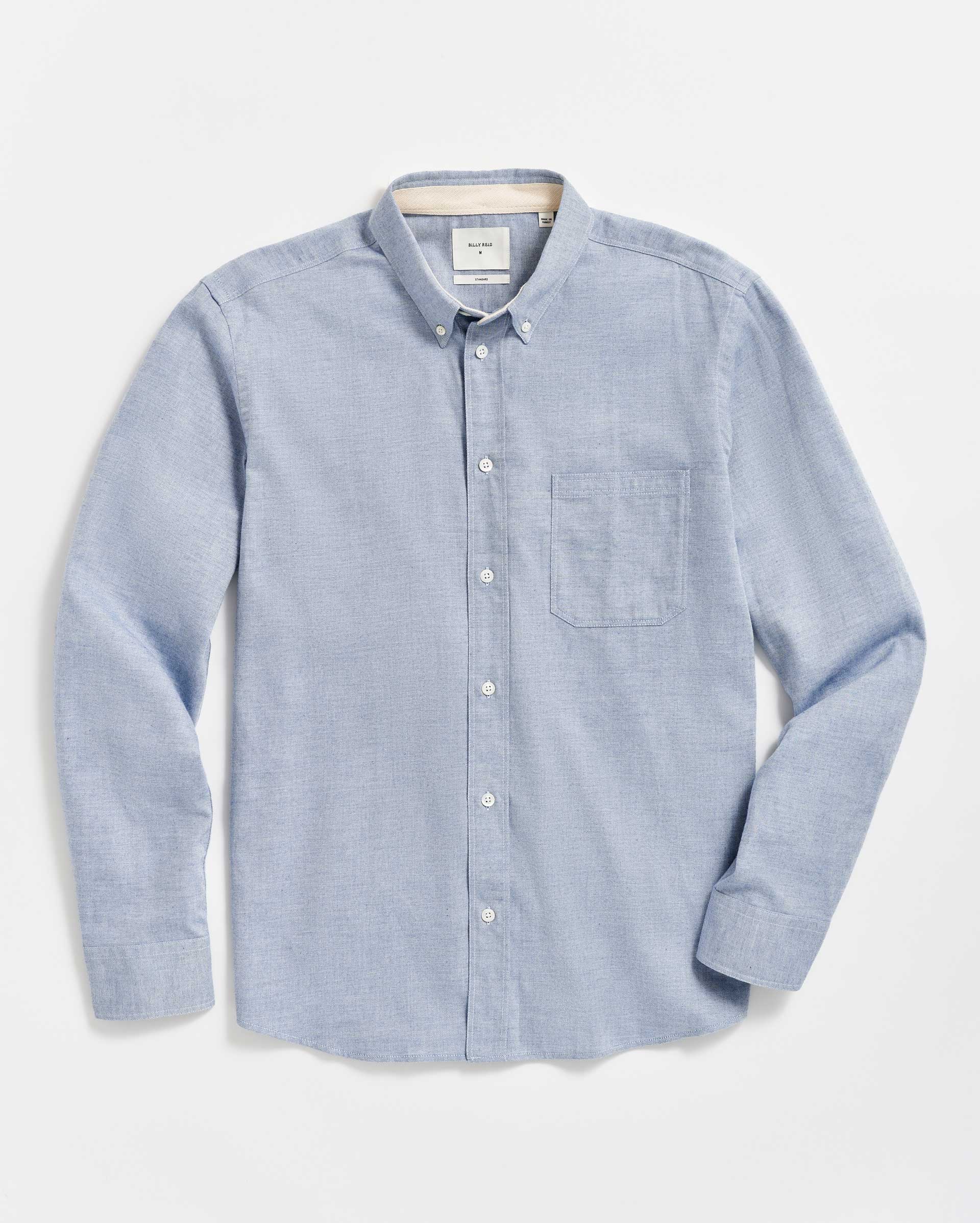 A light blue, long-sleeve button-down shirt with a collar and a front left chest pocket, neatly laid flat on a white background.