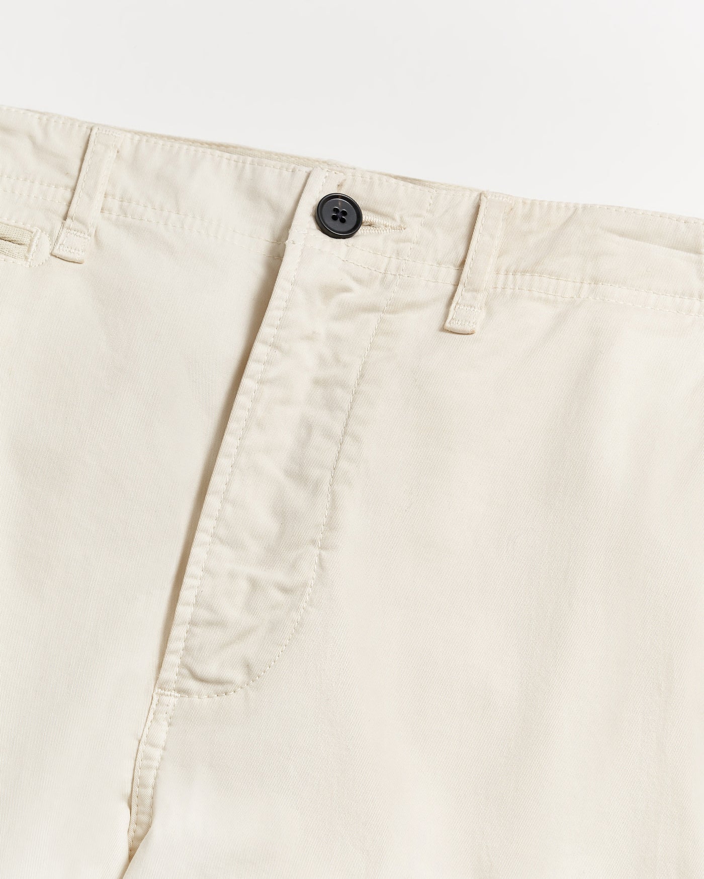 Close-up of a pair of light beige or off-white pants, showing the waistband, belt loops, black button, and part of the fly on a plain white background.