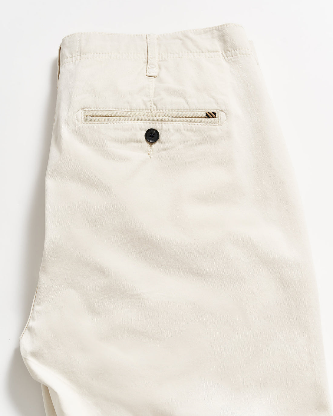 A pair of neatly folded beige pants, showing the back side with a single welt pocket featuring a black button, against a plain white background.