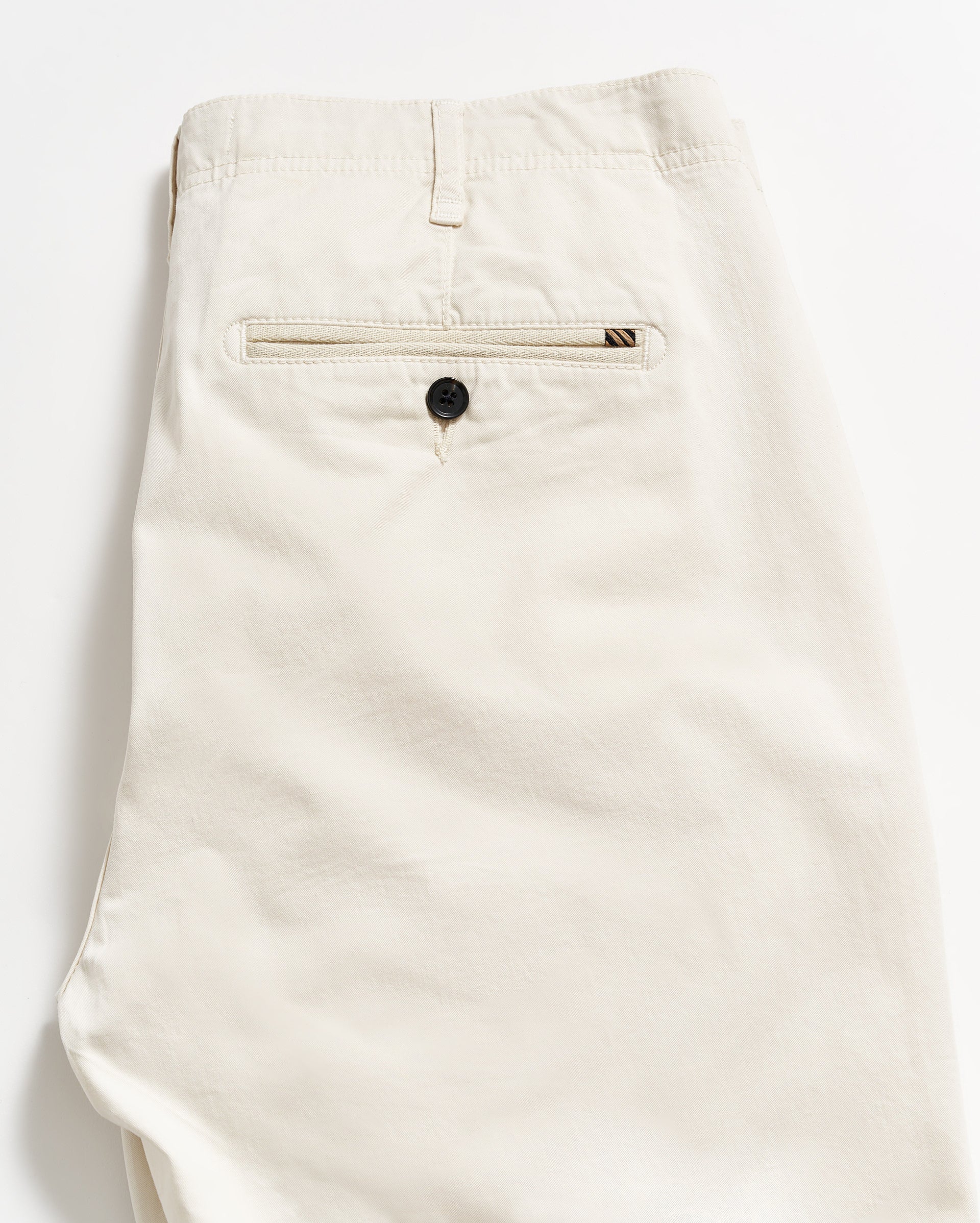 A pair of neatly folded beige pants, showing the back side with a single welt pocket featuring a black button, against a plain white background.