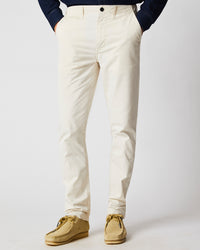 A person wearing off-white pants and tan suede shoes stands against a plain light background, with their hands in their pockets. Their upper body is partially visible, dressed in a dark long-sleeve shirt.