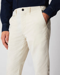 A person wearing ivory-colored pants with one hand in their pocket and a dark long-sleeve shirt, photographed from waist to mid-thigh.