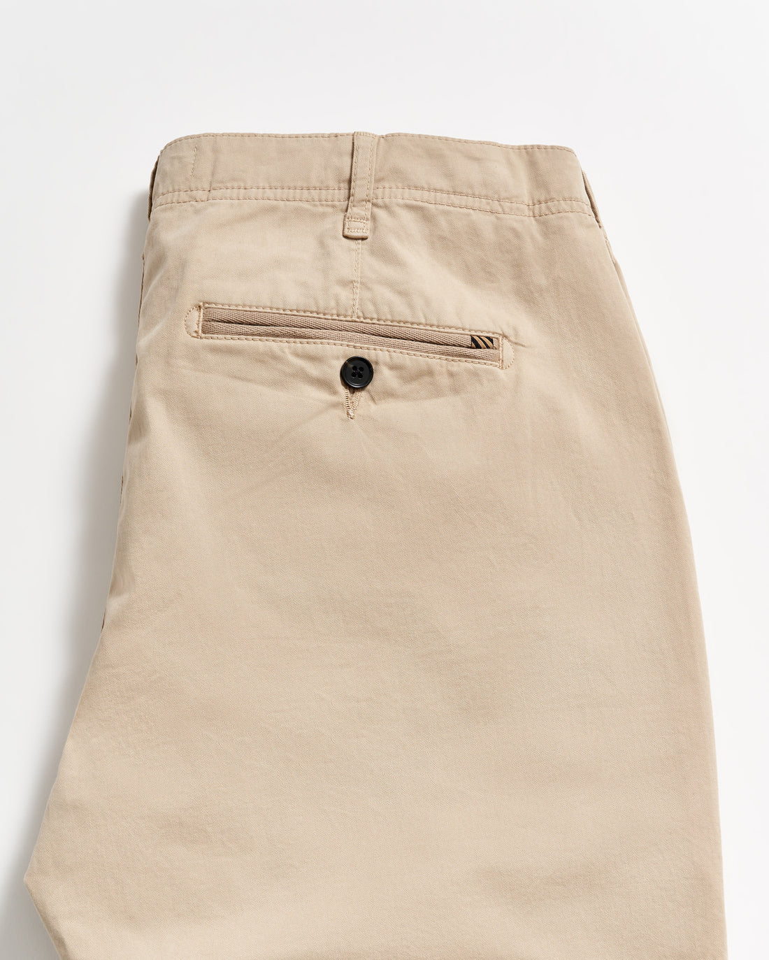 Beige khaki pants folded neatly, showing the back side with a single welt pocket featuring a black button. The fabric appears smooth, and there is a belt loop at the waistband.