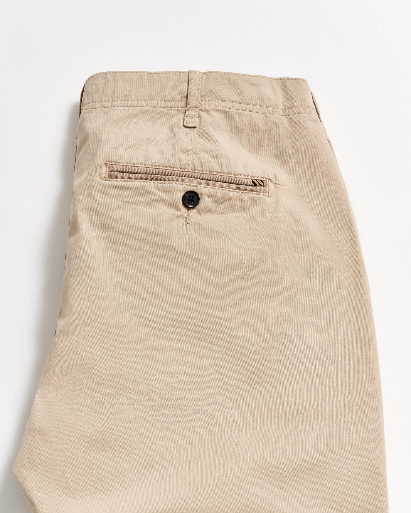 Beige khaki pants folded neatly, showing the back side with a single welt pocket featuring a black button. The fabric appears smooth, and there is a belt loop at the waistband.