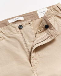 Close-up of beige slim cut trousers with the waistband partially opened, showing a button, zipper, and inner labels that read SLIM CUT and BILLY REID 32 against a white background.