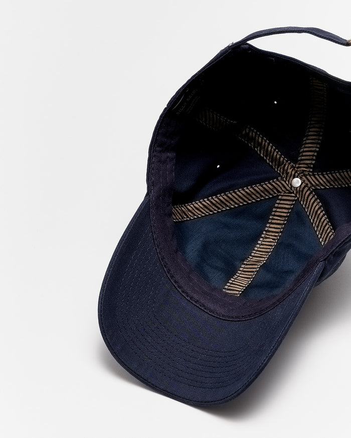 A navy blue baseball cap viewed from above, showing the inside with brown striped seams and a white button at the top center. The cap is positioned on a plain white surface.